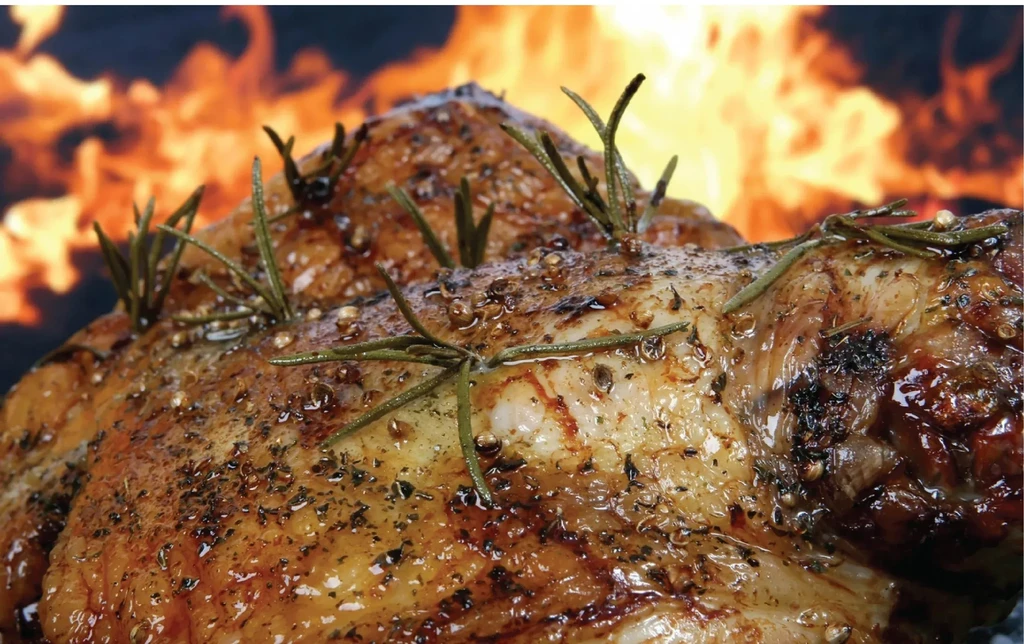 Golden-brown roasted meat, seasoned with rosemary and peppercorns, fire-cooked.