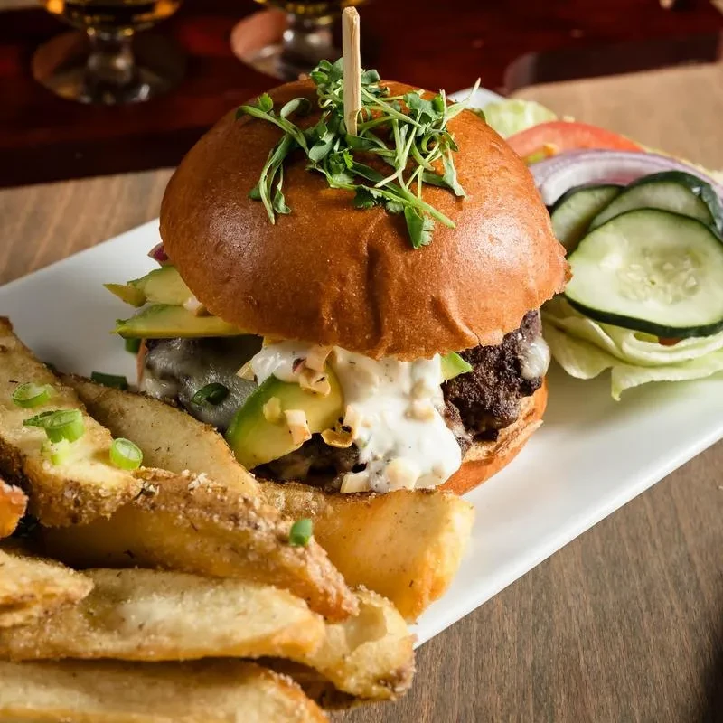 Gourmet burger with avocado, potato wedges, and a side salad.
