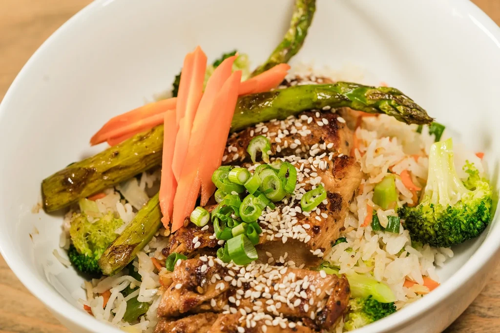 Sliced chicken, rice, broccoli, carrots, asparagus, and sesame seeds.