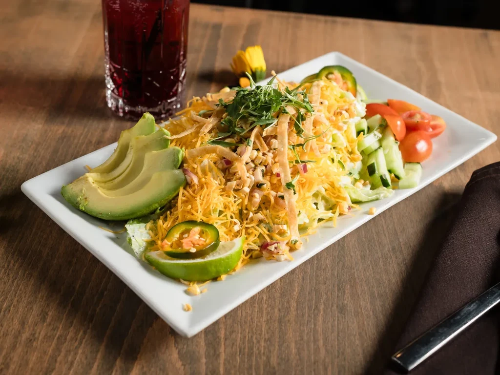 Vibrant salad with avocado, cheese, tomatoes, cucumbers on white plate.