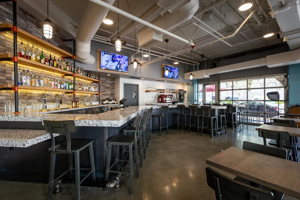 Modern industrial bar interior with sports visible on two TVs.