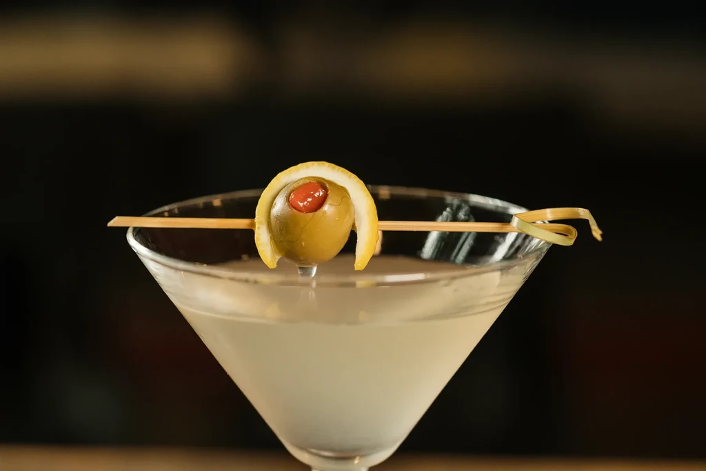 Cloudy off-white martini with olive, pimento, and twisted lemon peel.