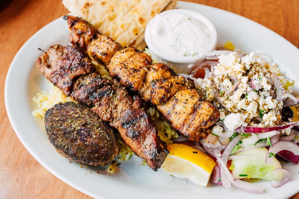 Mediterranean platter with grilled meats, rice, pita, tzatziki, and feta salad.