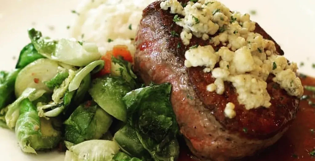 Seared steak topped with blue cheese, herbs, brussels sprouts, and mashed potatoes.