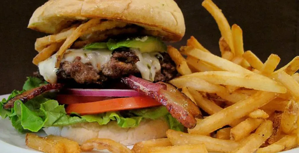 Burger with melted cheese, avocado, bacon, lettuce, and golden fries.