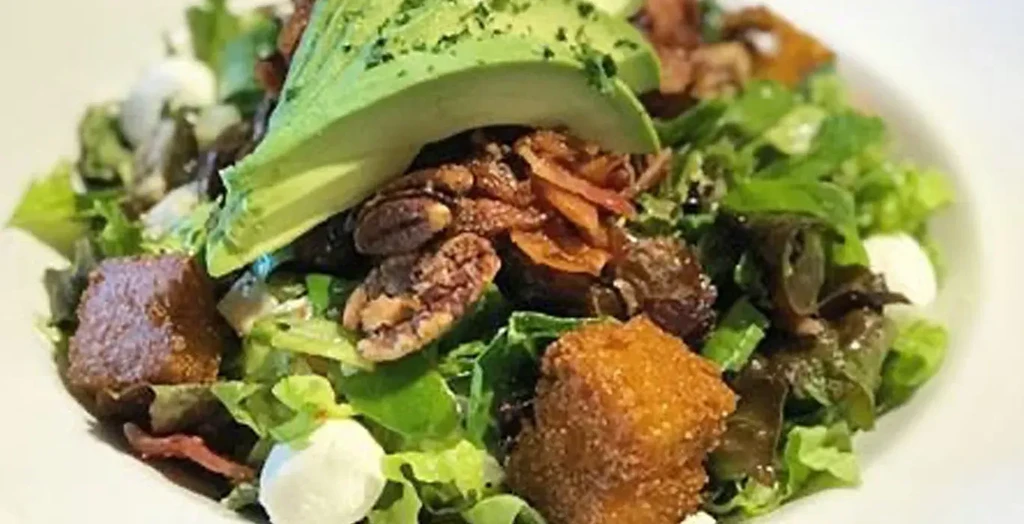 Overhead salad with avocado, golden cheese, bacon, pecans, and greens.