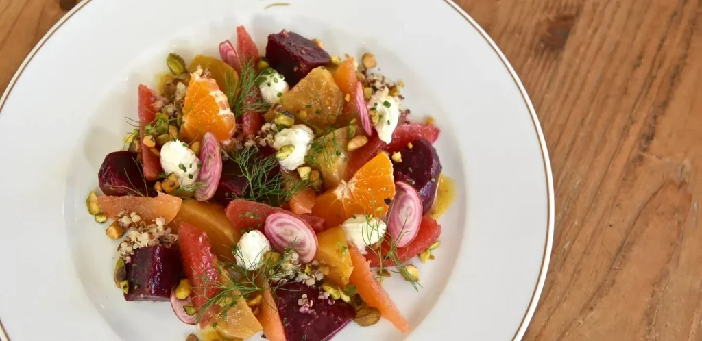 Vibrant salad with beets, citrus, cheese, pistachios, on white plate.