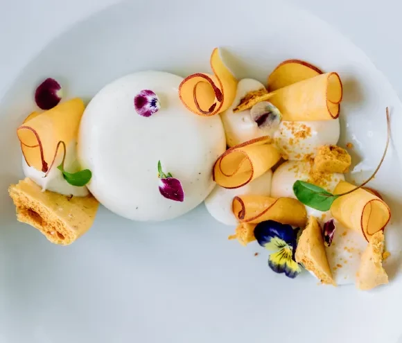 Plated dessert with white mousse, honeycomb, fruit crisps, and edible flowers.