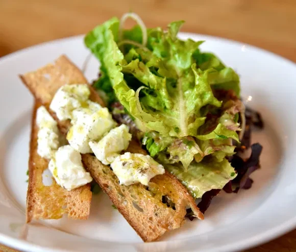 Plate of green salad with cheese-topped toasted bread.