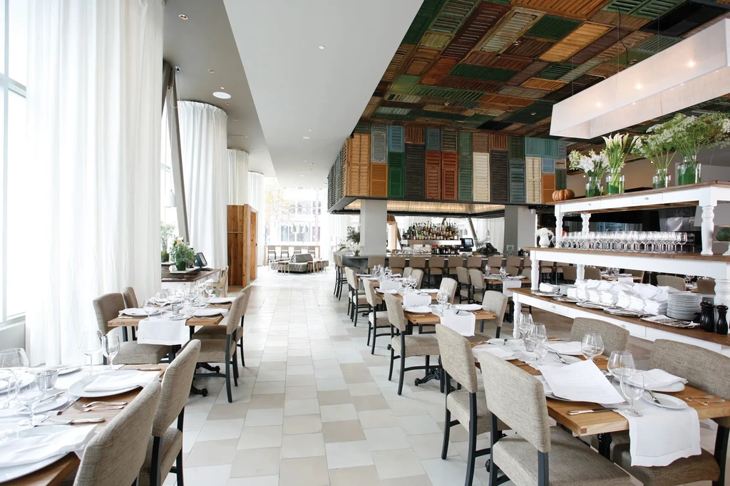 Modern restaurant interior with set tables, bar, and unique mosaic ceiling.