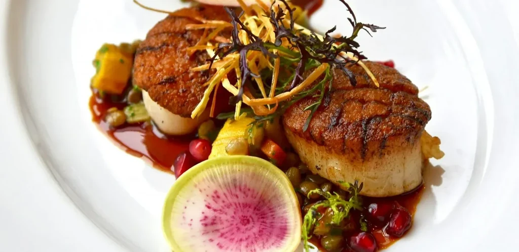 Seared scallops, colorful accompaniments, watermelon radish, sauce, and garnish.