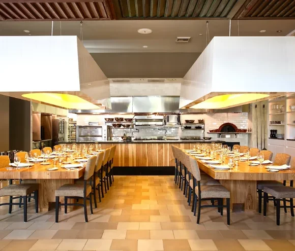Empty modern restaurant with set communal tables and an open kitchen.