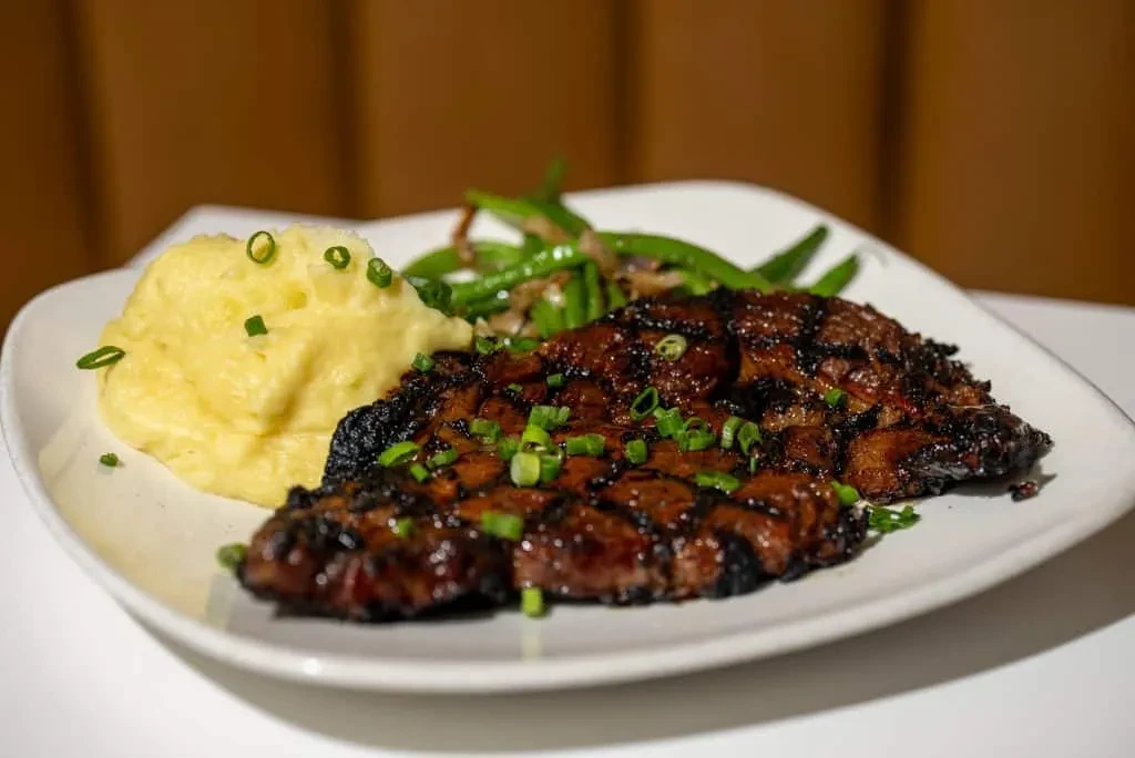 Grilled steak, mashed potatoes, green beans, garnished with green onions.