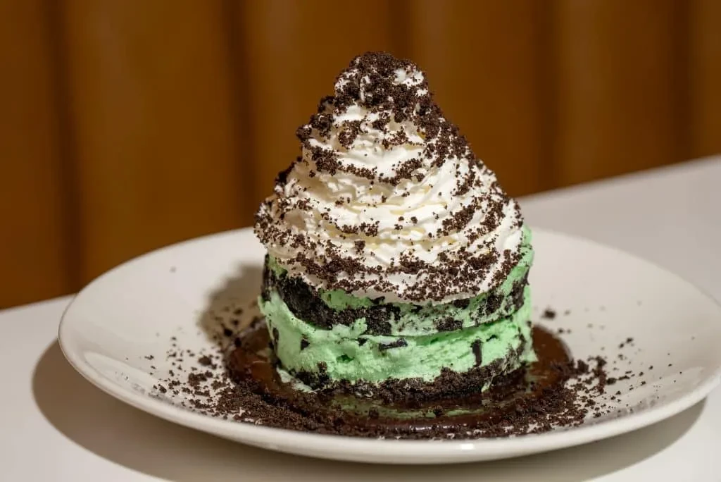 Towering mint chocolate chip dessert with whipped cream and chocolate sauce.