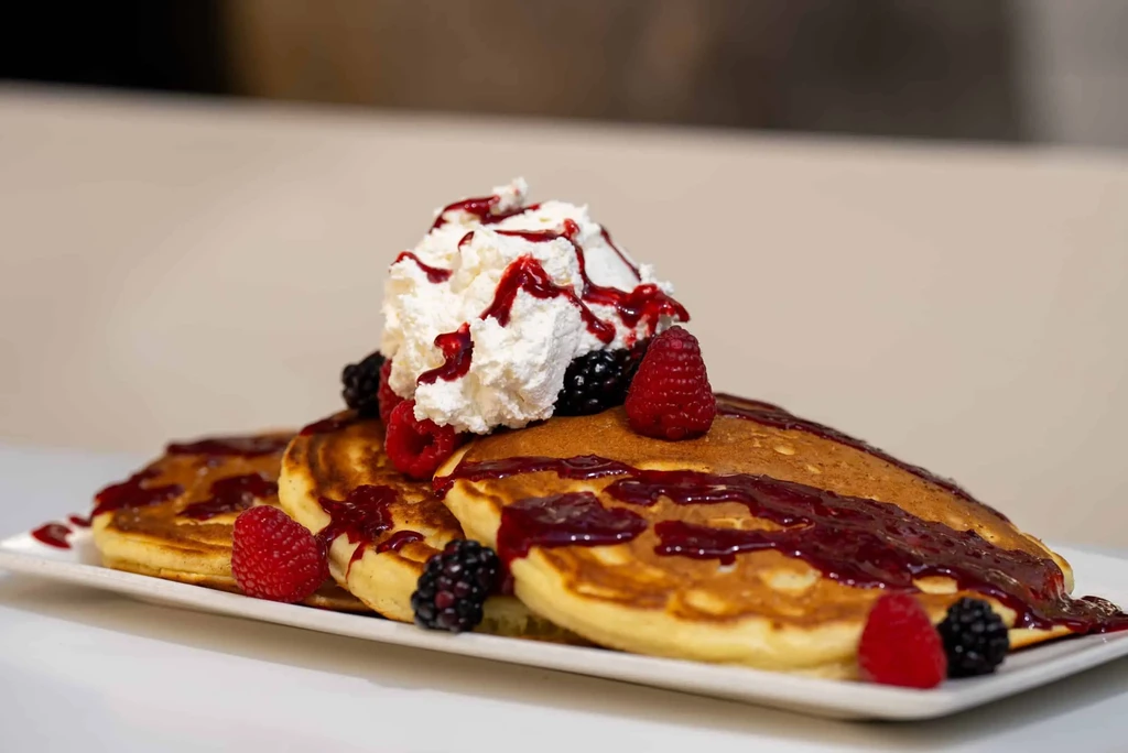 Stack of pancakes with berry sauce, whipped cream, and fresh berries.