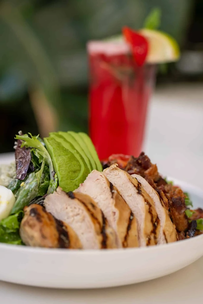 Close-up of colorful grilled chicken salad, avocado, and red drink.