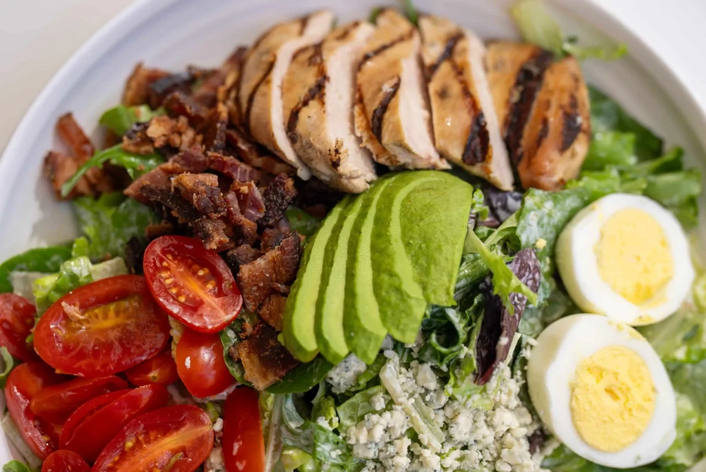 Colorful salad with grilled chicken, bacon, avocado, tomatoes, and eggs.