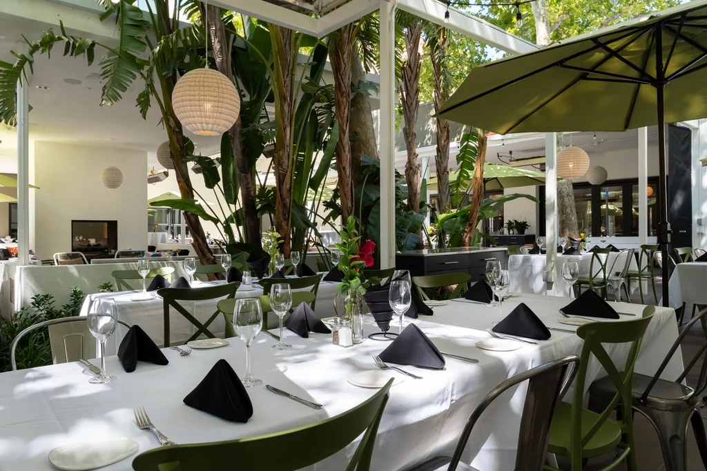Lush tropical dining area with set tables under a pergola.