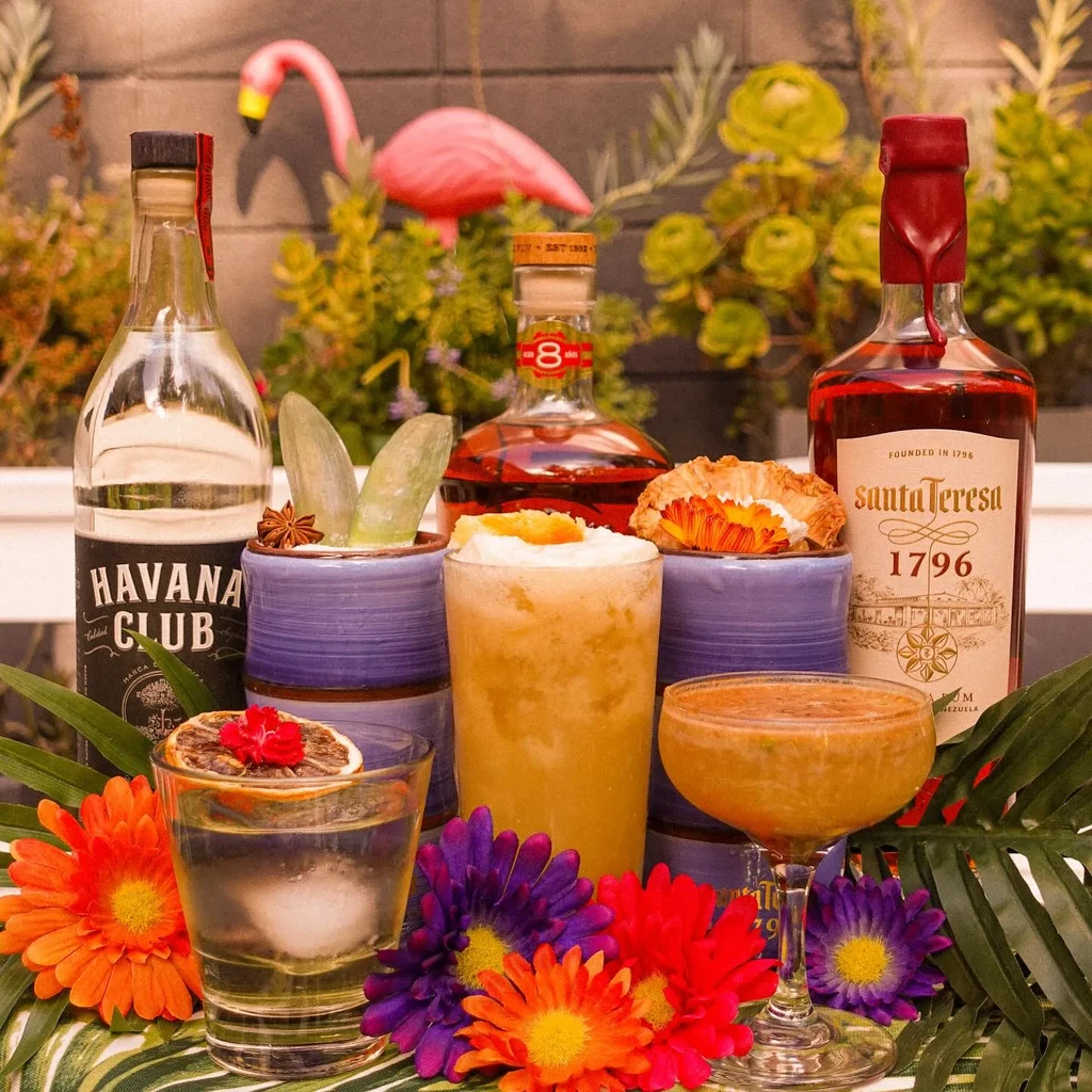 Tropical cocktail arrangement with rum bottles, flowers, and flamingo ornament.