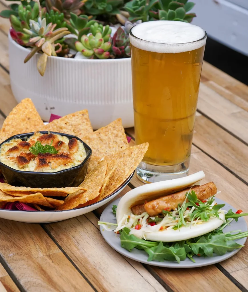 Creamy dip, chips, beer, deconstructed bao bun on rustic table.