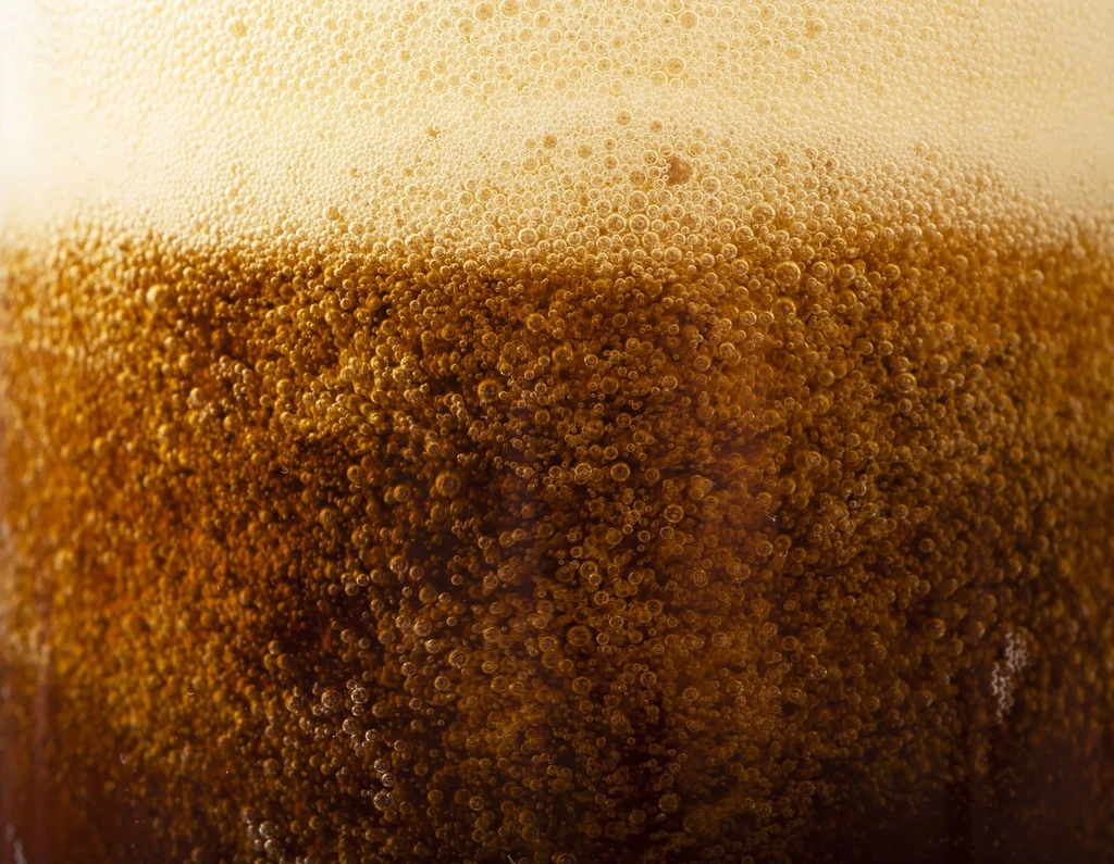 Abstract macro of amber carbonated beverage with golden foam and rising bubbles.