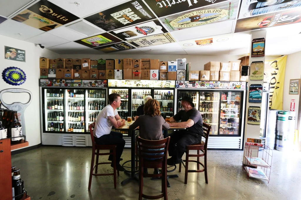 Modern beer bar: three people, large fridges full of beer.