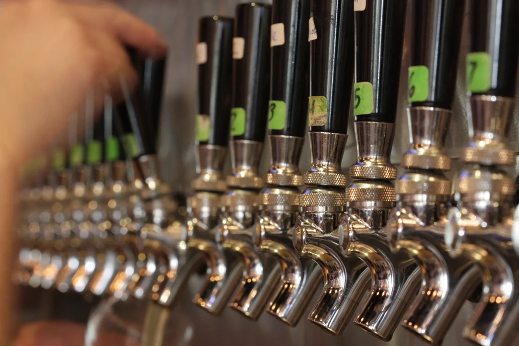 Row of shiny beer tap handles with numbered labels and a reaching hand.