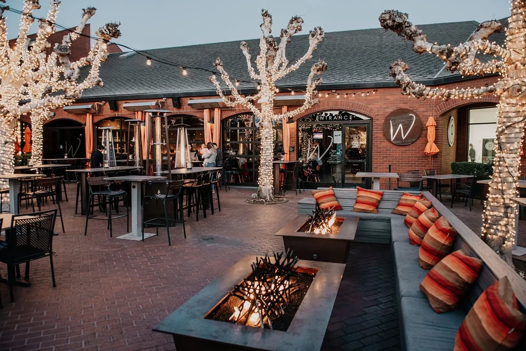 Outdoor restaurant patio with fire pits, twinkling lights, and dining guests.