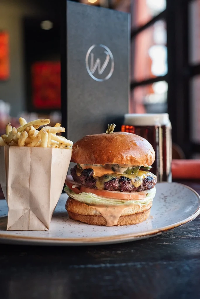 Well-constructed gourmet burger and fries with beer and menu.