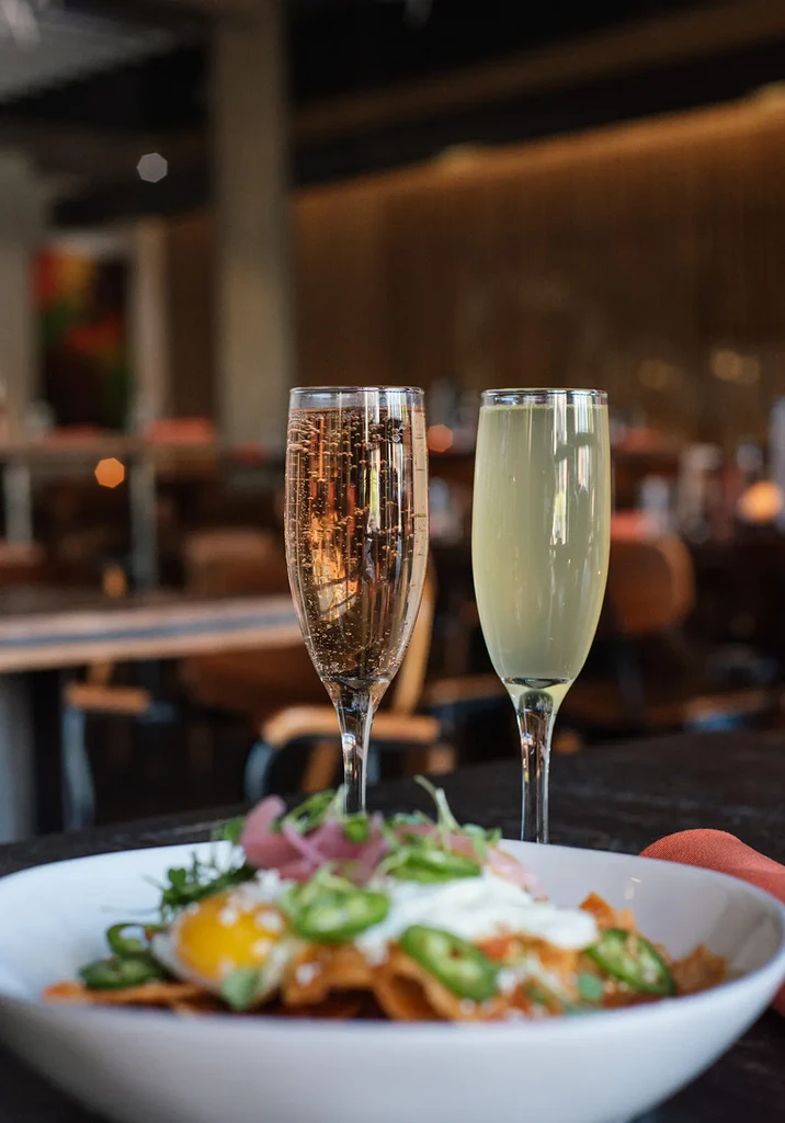 Colorful breakfast dish with fried eggs, two champagne flutes, restaurant setting.
