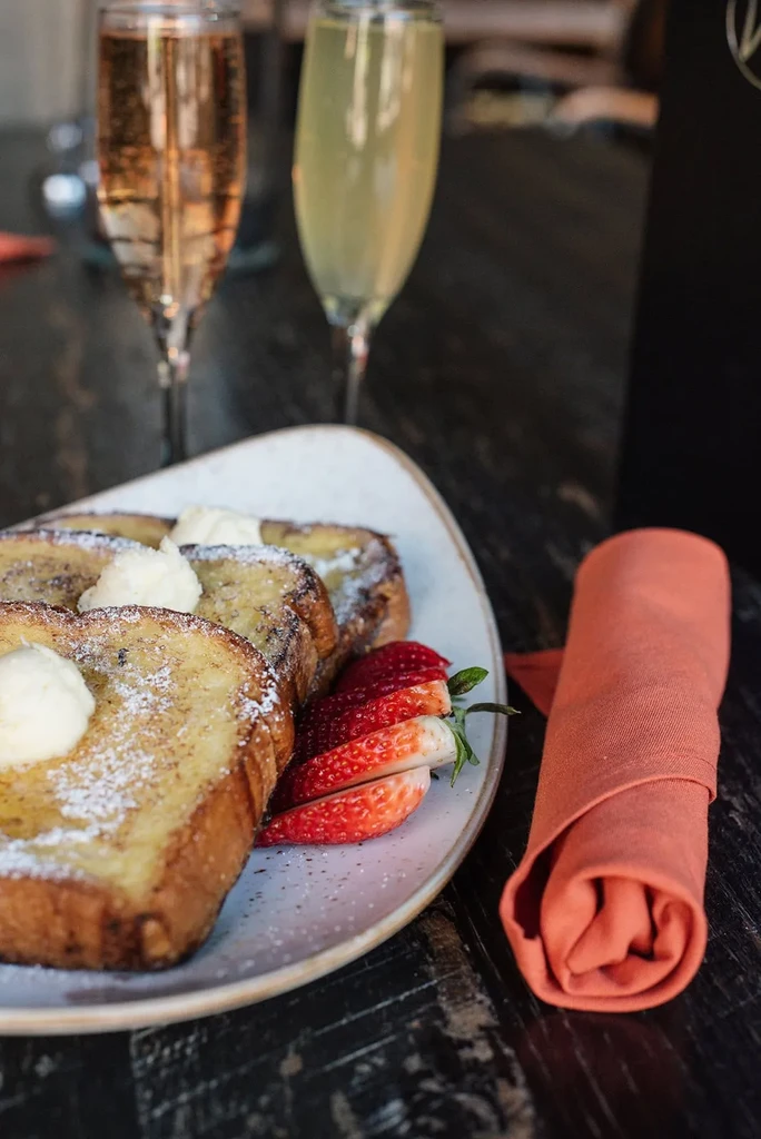 Golden French toast with powdered sugar, strawberries, and blurred cocktails.