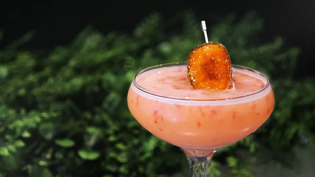 Pale orange cocktail with foam and caramelized fruit in coupe glass.
