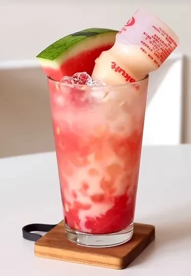 Layered watermelon drink with inverted Yakult bottle and watermelon slice.