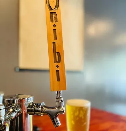 Close-up of chrome beer tap with UBI-carved wooden handle and blurred beer.