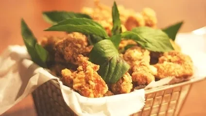 Crispy fried chicken or appetizers garnished with basil in a basket.