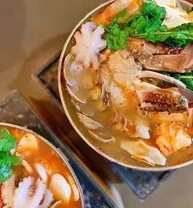 Two metal pots of seafood hot pot with various seafood and greens.