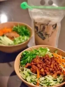 Colorful bowl of food, second blurry bowl, and boba tea drink.