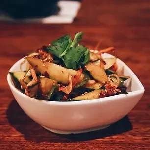 Cucumber and vegetable salad with chili and cilantro in a white bowl.
