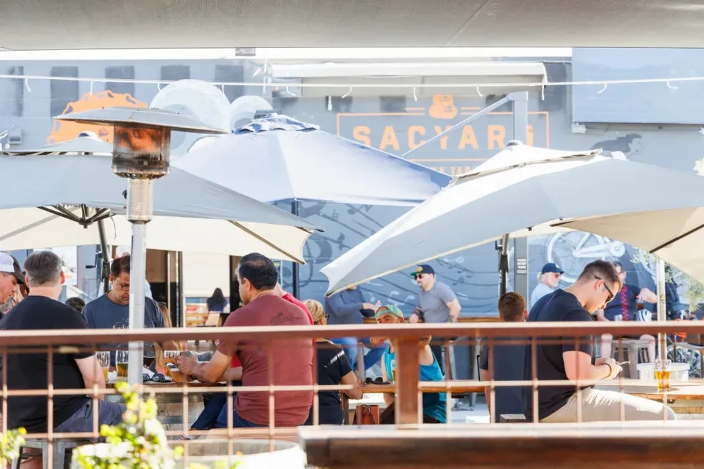 Sunny outdoor patio with patrons, drinks, and large umbrellas.