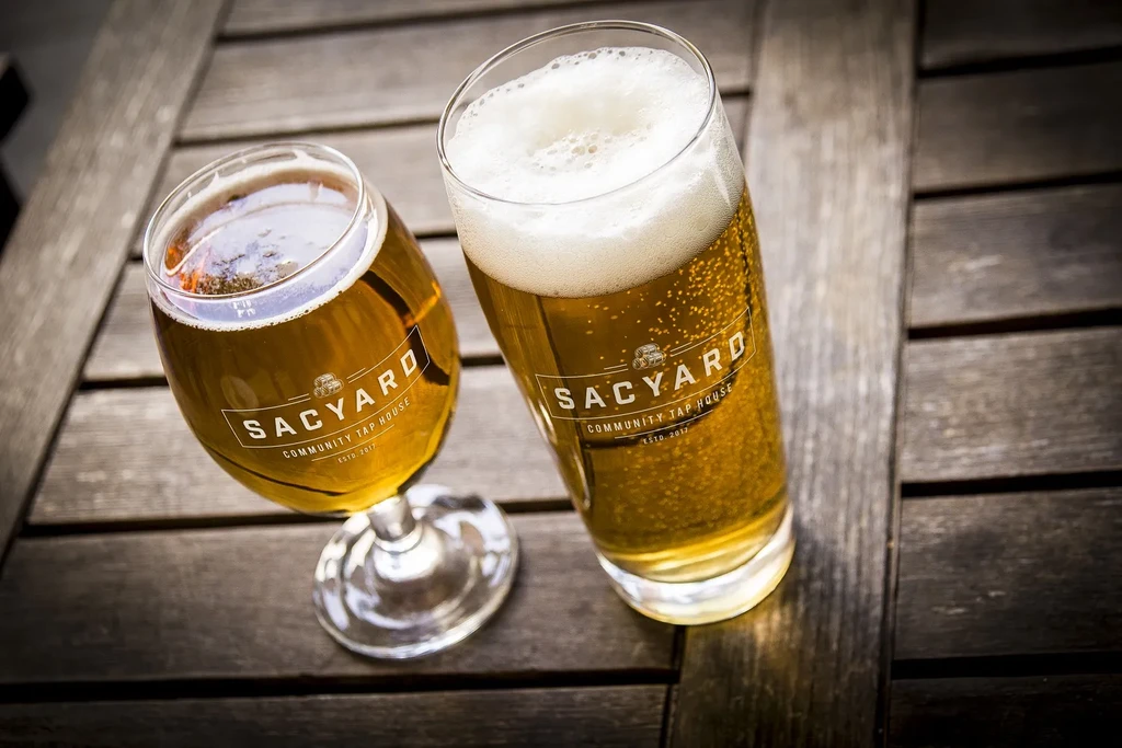 Two SACYARD beers, one pint and one tulip, on a wooden table.
