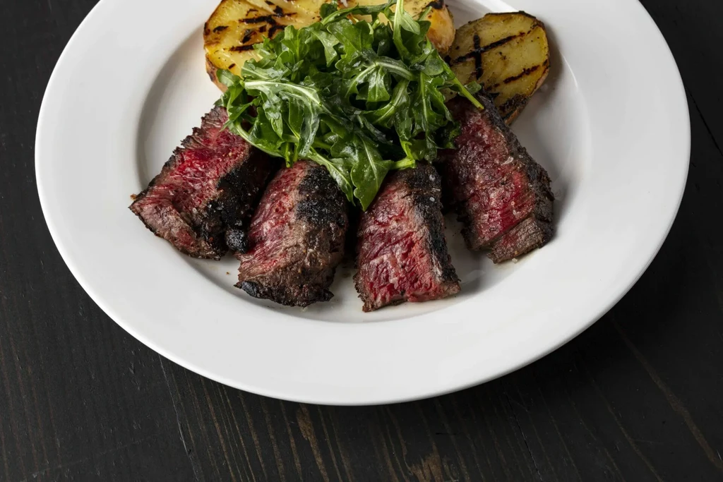 Sliced medium-rare steak with arugula and grilled potatoes on a white plate.