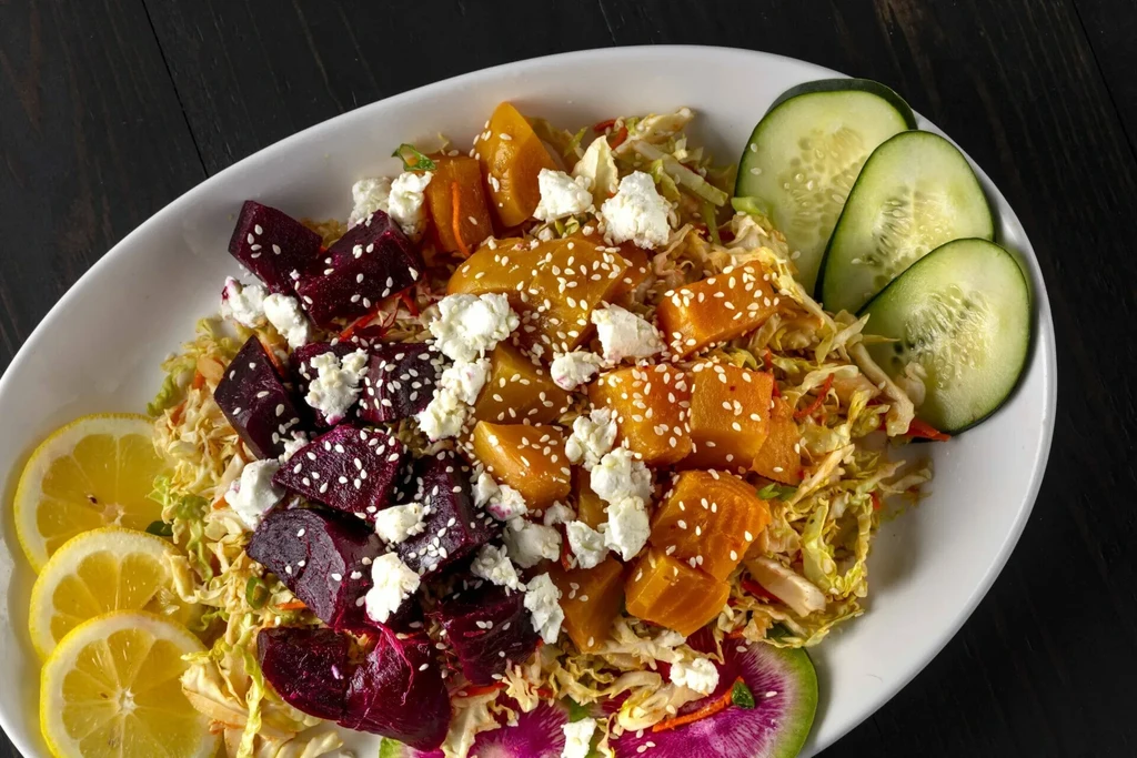 Colorful salad with beets, root vegetables, cheese, greens, and fresh garnishes.