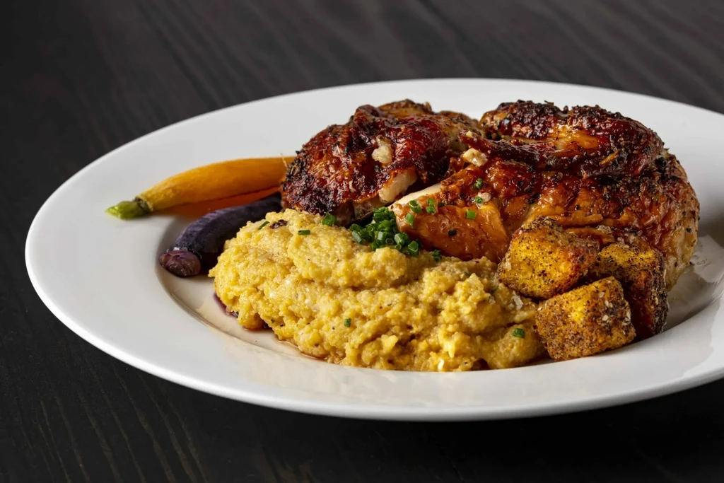 Plated roasted chicken, polenta, carrots, and roasted root vegetables.
