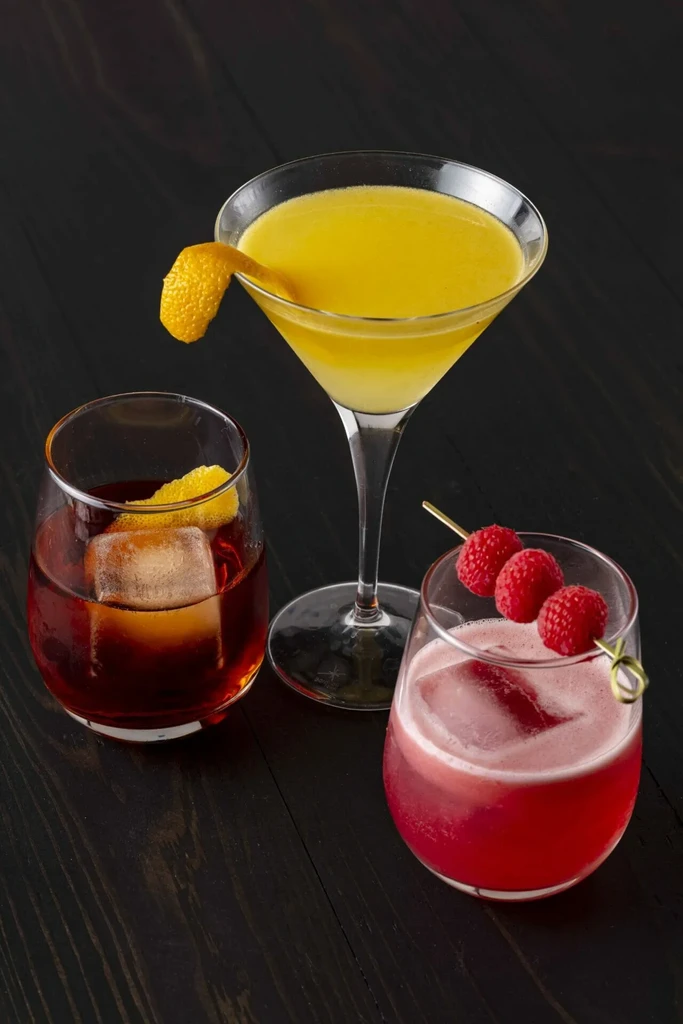 Three garnished cocktails in stemless and martini glasses on dark surface.