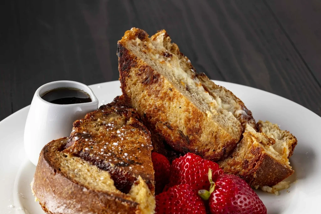 Thick French toast, strawberries, dark syrup, and powdered sugar on a plate.