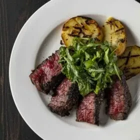 Overhead close-up of sliced medium-rare steak, greens, and grilled potatoes.