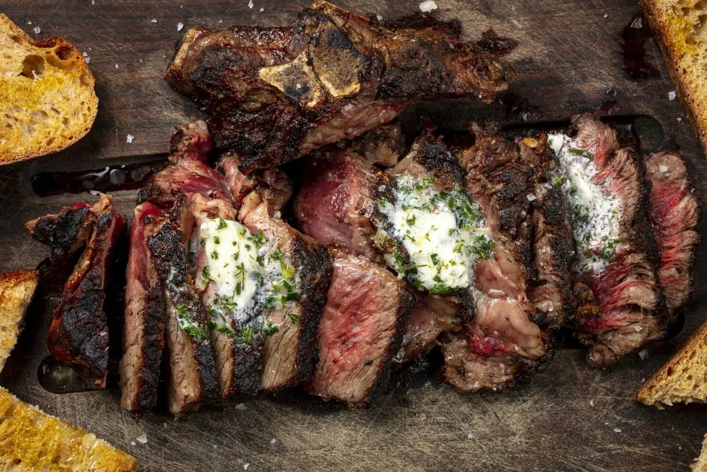 Sliced medium-rare steak with melting herb butter on a rustic board.