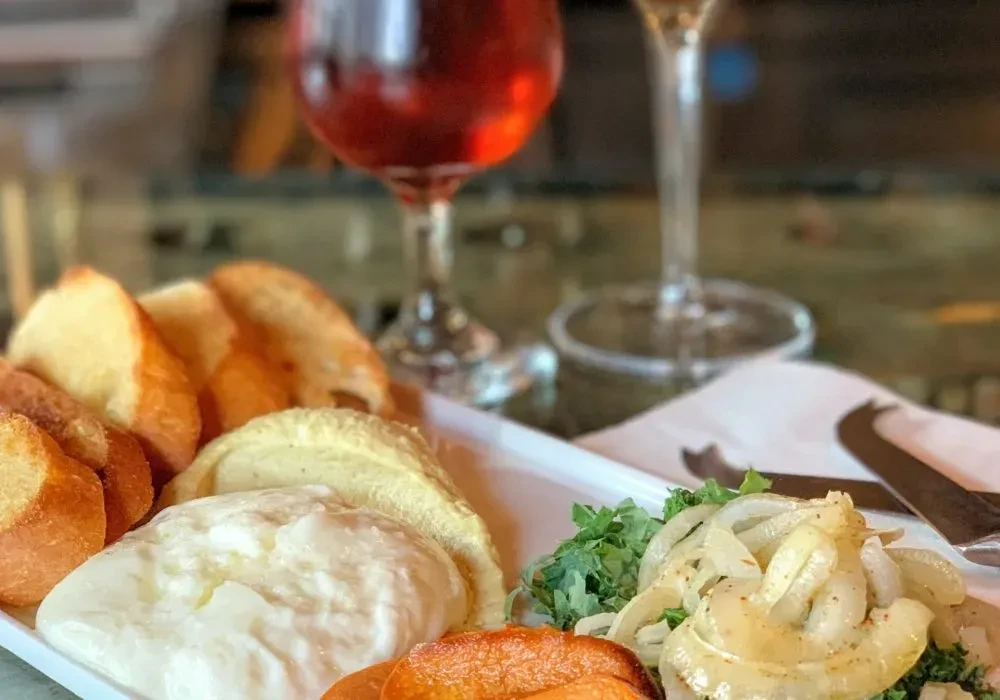 Tapas platter with bread, creamy dips, sautéed onions, and wine glasses.