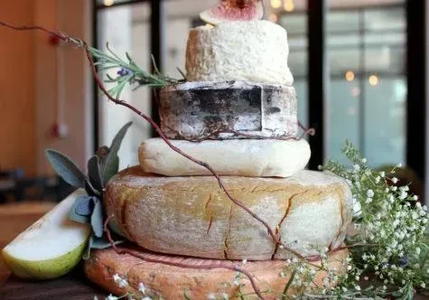 Tiered cheese tower adorned with fig, pear, herbs, and flowers.