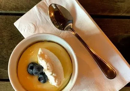 Close-up: Golden custard with cream, blueberries, spoon on wooden table.